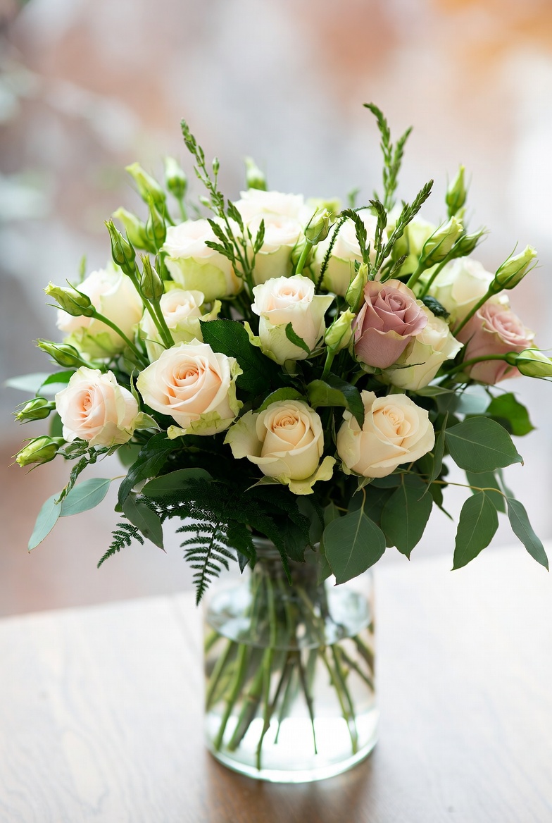 Свежий букет из роз и зелени в стеклянной вазе на деревянном столе